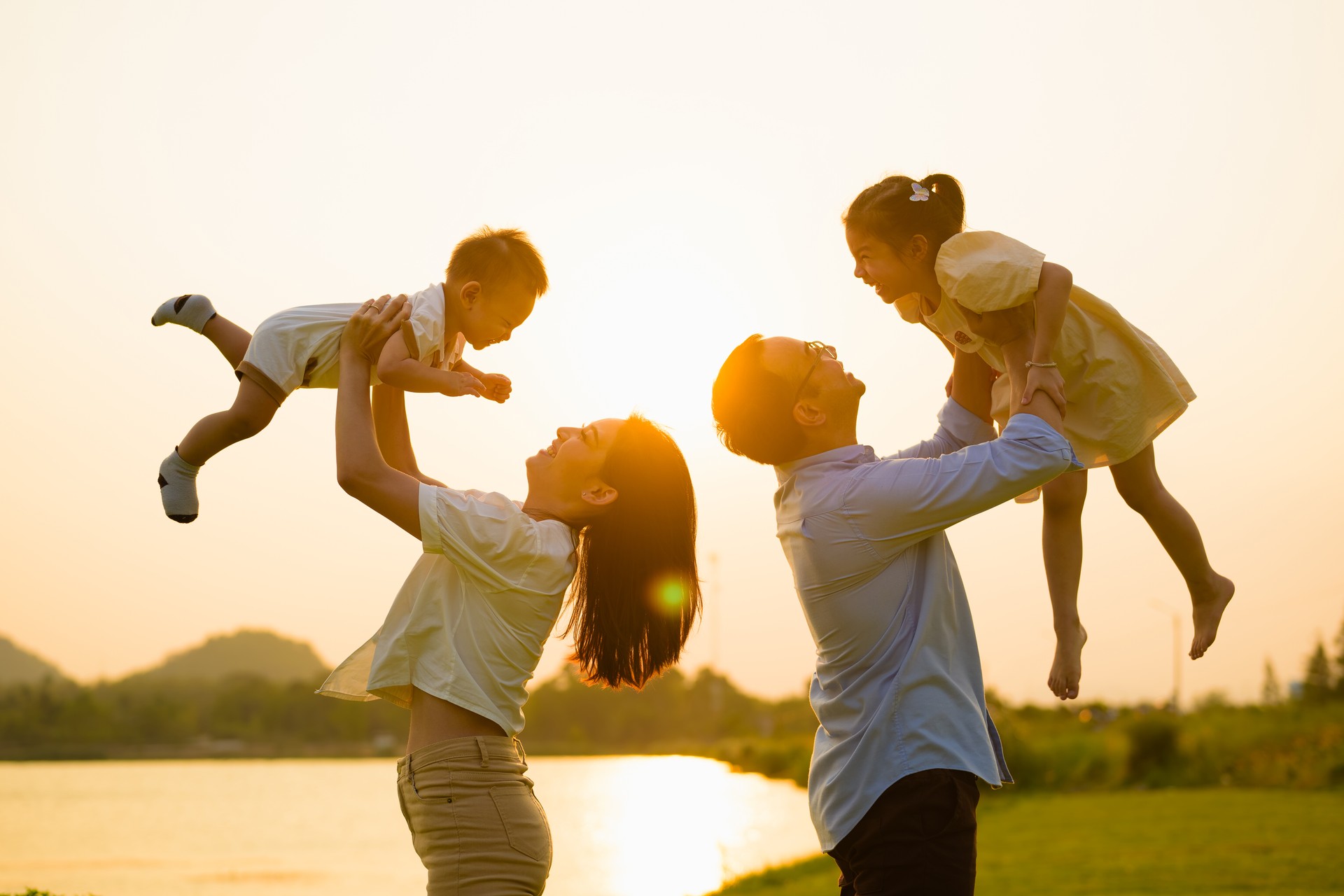 Father and mother holding children playing together in park in evening